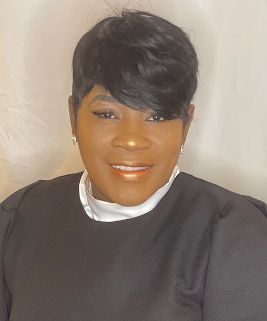 Picture of Carolyn Lewis after breast cancer treatment. Carolyn is sporting short haircut where black robe with white collar.